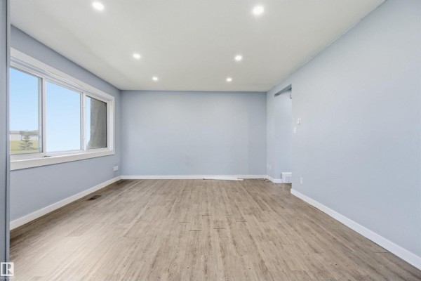 Spacious living room with light blue walls, recessed lighting, and a large window. - 13223 85 St Nw, Edmonton