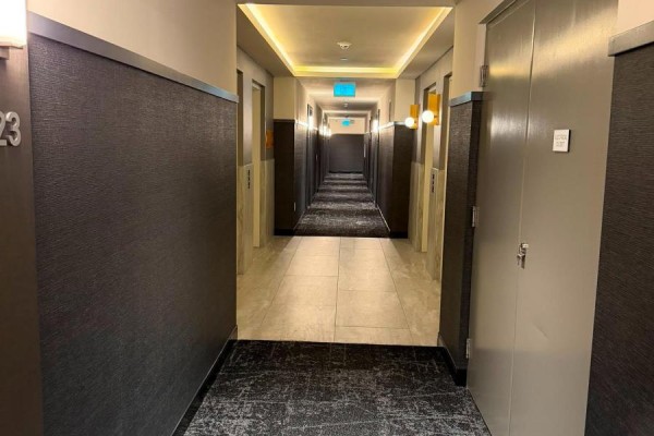 View down a long, well-lit apartment building hallway with multiple doors on either side. - 1323 - 2485 Eglinton Avenue W, Mississauga