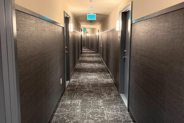 Perspective view down a curved apartment hallway lined with dark textured wallpaper and doors. - 1323 - 2485 Eglinton Avenue W, Mississauga