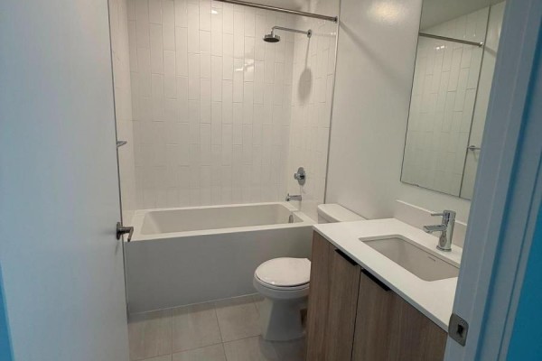 A compact bathroom with a white bathtub, toilet, and a light wood vanity with a white countertop. - 1323 - 2485 Eglinton Avenue W, Mississauga