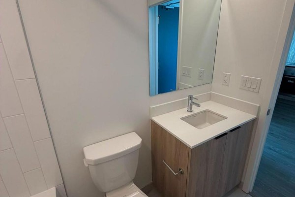 Close-up of a bathroom vanity with a white sink, faucet, and wood cabinet doors. - 1323 - 2485 Eglinton Avenue W, Mississauga