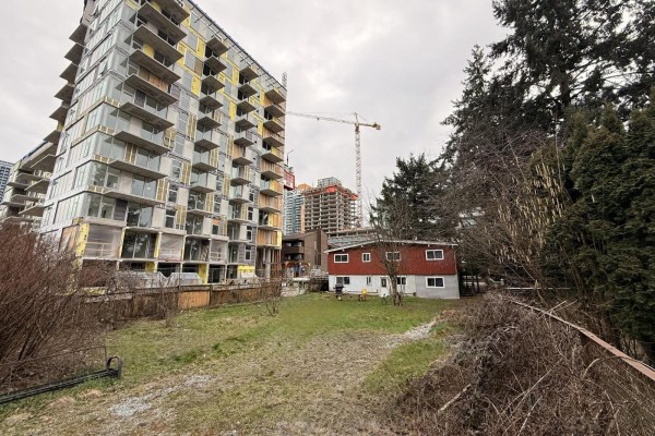 Backyard view of red house with grass and trees, construction in the background. - 13231 104a Avenue, Surrey
