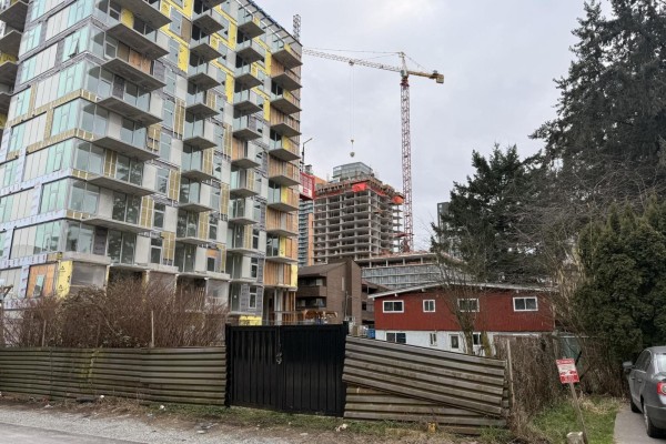 View of red house with construction cranes and buildings nearby, fenced area in front. - 13231 104a Avenue, Surrey