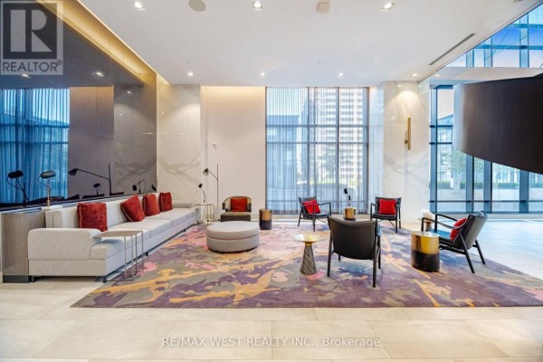 Lobby seating area with a long grey sofa, accent chairs, and a colorful rug. - 1327 - 5 Mabelle Avenue, Toronto