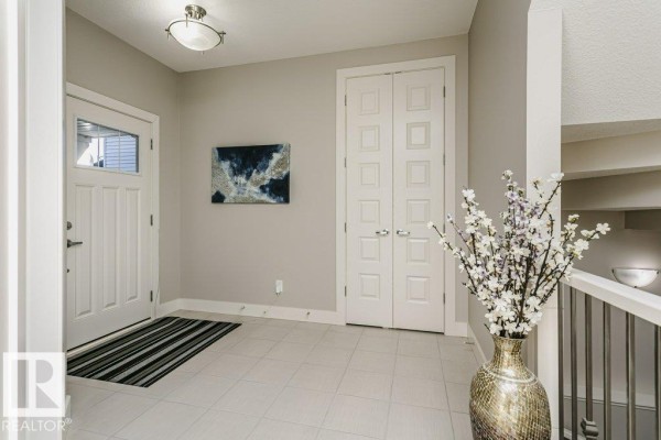 Entrance foyer with light grey walls, a white door, black and white striped rug, and double doors leading further into the house. - 1327 158 St Sw, Edmonton