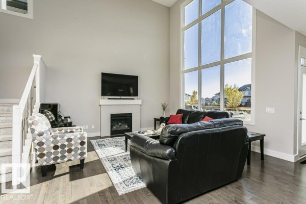 Living room with a high ceiling, large windows, a gas fireplace with a white mantel, and black leather sofas. - 1327 158 St Sw, Edmonton