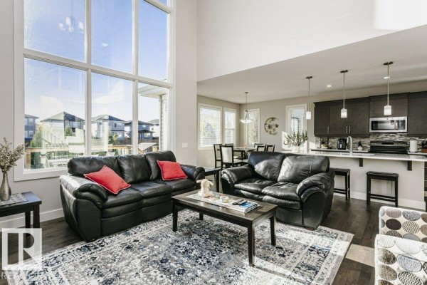 Living room with black leather sofas, a large window, open concept to the kitchen and dining area with dark cabinets. - 1327 158 St Sw, Edmonton