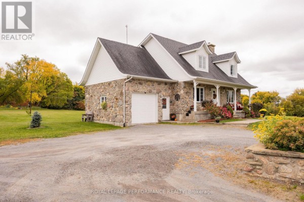 Side view of the stone house showing the attached garage, porch, and surrounding lawn. - 1327 County Road 34 Road, North Glengarry