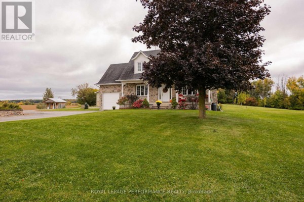 View of the stone house from the front right lawn, with a large dark tree in the foreground. - 1327 County Road 34 Road, North Glengarry