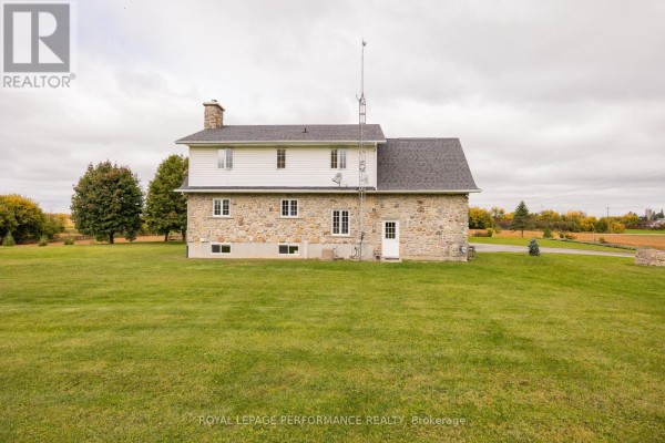 Rear view of the two-story stone and white vinyl siding house with a chimney and lawn. - 1327 County Road 34 Road, North Glengarry