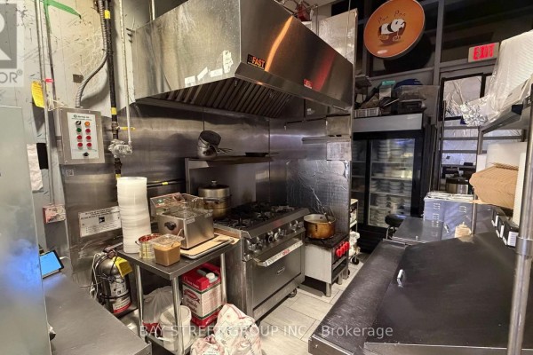 Commercial kitchen with stainless steel stove, deep fryer, exhaust hood, and refrigerator unit. - 133 - 4750 Yonge Street, Toronto