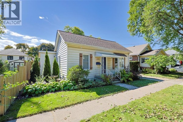 Side view of the beige bungalow at 133 Bright Street, showing the front yard and sidewalk. - 133 Bright Street, Sarnia