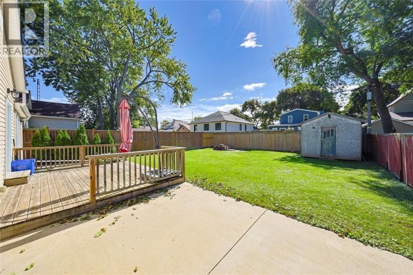 Backyard of the property with a wooden deck, concrete patio, grassy lawn, and shed. - 133 Bright Street, Sarnia