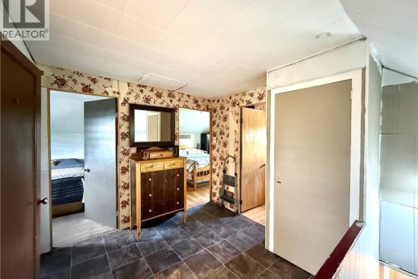 A hallway with floral wallpaper, a vintage dresser, and doorways leading to bedrooms. - 133 Chemin F. Bernier Road, Saint Joseph De Madawaska