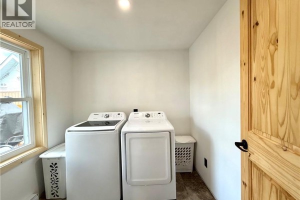 A laundry room with white washer and dryer units, a wooden door, and a window overlooking the exterior. - 133 Chemin F. Bernier Road, Saint Joseph De Madawaska