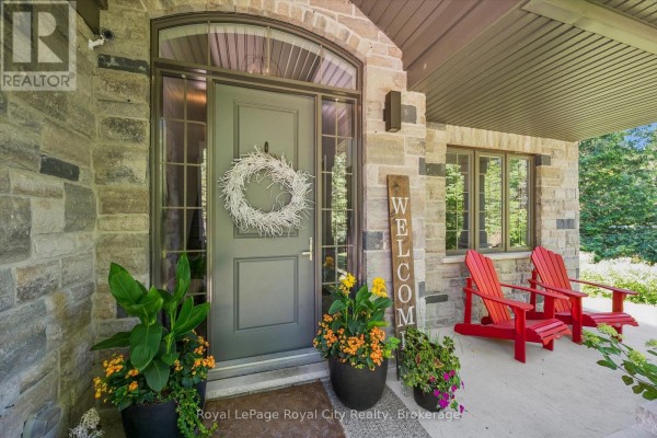 Covered front porch with stone pillars, grey front door, two red Adirondack chairs, and potted plants. - 133 Cooks Mill Road, Puslinch