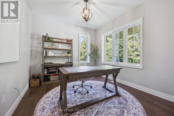 Home office with a large wooden desk, rolling chair, bookcase, and large windows overlooking trees. - 133 Cooks Mill Road, Puslinch