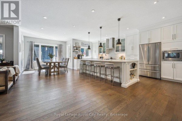 Open-concept kitchen and dining area with white cabinets, island with bar stools, wooden dining table, and hardwood floors. - 133 Cooks Mill Road, Puslinch