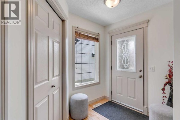 Foyer with a white door, window with ornate glass, closet doors, and hardwood flooring. - 133 Everwoods Close Sw, Calgary