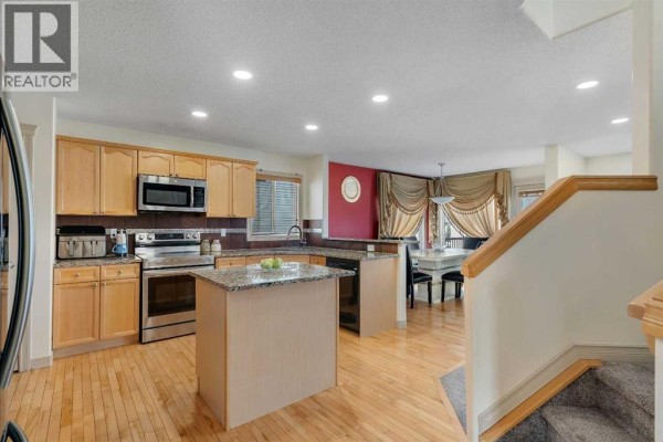 Kitchen with light wood cabinets, stainless steel appliances, granite countertops, and an island. - 133 Everwoods Close Sw, Calgary