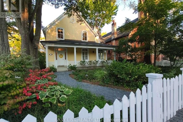 Path through garden with red and green plants leading to a yellow house with a white porch. - 133 Main Street, Markham