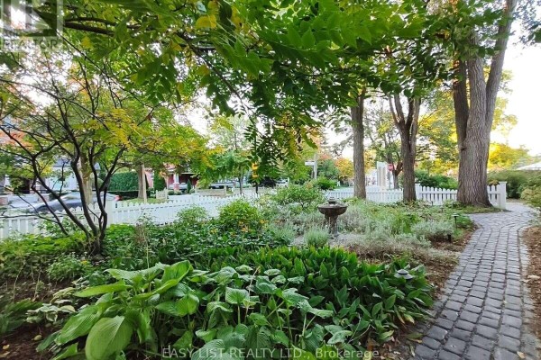 Cobblestone path through a garden with large green hosta plants and a bird bath. - 133 Main Street, Markham