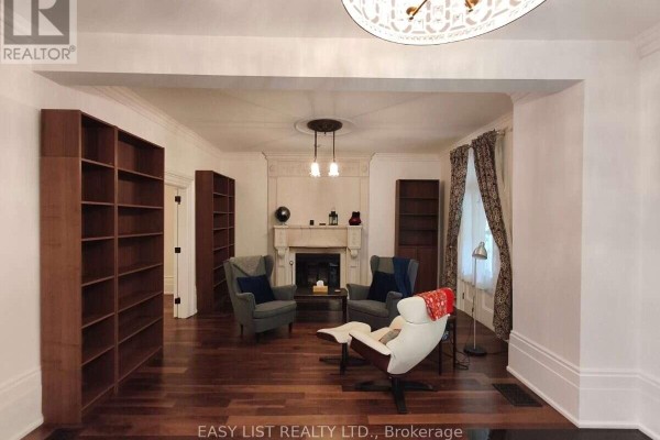 Living room with hardwood floors, floor-to-ceiling bookshelves, gray armchairs, and a stone fireplace. - 133 Main Street, Markham