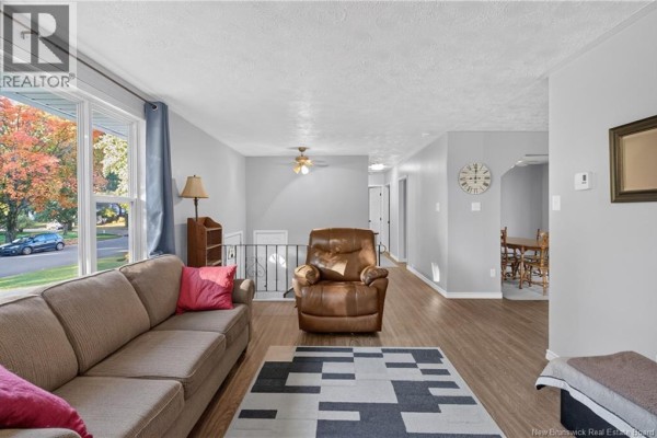 Living room with a beige sofa, brown leather recliner, and a geometric rug. - 133 Willis Street, Fredericton