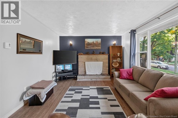 Living room with a stone fireplace, television, and large windows. - 133 Willis Street, Fredericton