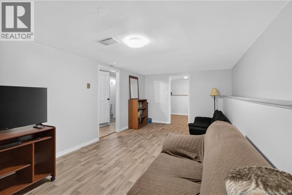 Basement living area with light grey walls, wood-look flooring, and a sofa. - 133 Willis Street, Fredericton