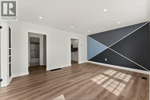 Living room with a sectional sofa, blue armchair, coffee table, and a modern geometric accent wall with a TV. - 1330 Central Avenue, Windsor