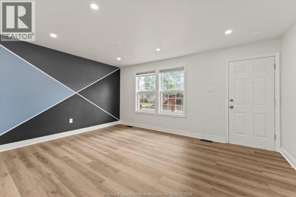Open-concept living space with wood-look flooring, white walls, and a view into a bathroom and kitchen area. - 1330 Central Avenue, Windsor