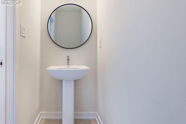 Small powder room with white pedestal sink, chrome faucet, and a round black-framed mirror on a white wall. - 1330 Shevchenko Boulevard, Oakville