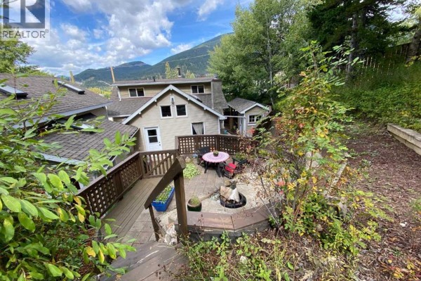 Front view of a light beige house with tan siding and a garden with flowers and rocks in the foreground. - 13302 15 Avenue, Blairmore