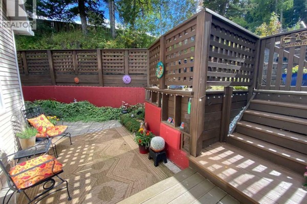 Backyard patio with red concrete walls, wooden privacy screens, and outdoor seating with decorative items. - 13302 15 Avenue, Blairmore
