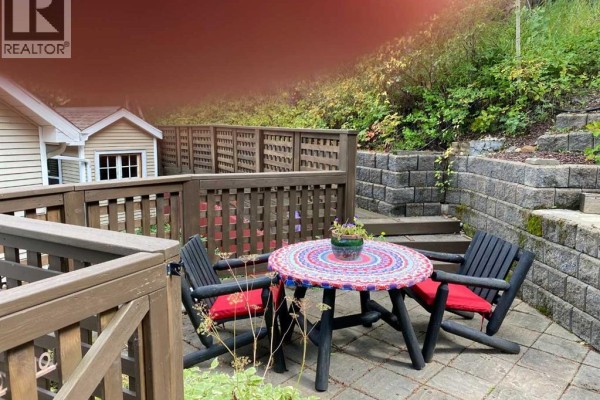 Outdoor patio with a round table, two chairs with red cushions, and a stone retaining wall behind. - 13302 15 Avenue, Blairmore