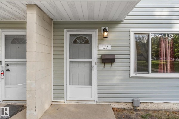 Close-up of a white townhouse front door with a screen door and a black mailbox. - 13307 89a St Nw, Edmonton