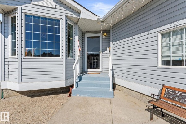 Detail of the front door steps and entryway of a light blue house with a bench. - 13308 155 Av Nw, Edmonton