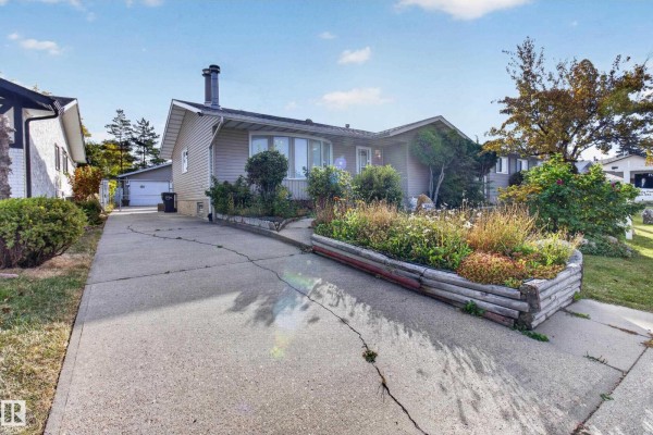 Concrete driveway leading to the side of a beige bungalow with attached garage. - 13315 30 St Nw, Edmonton