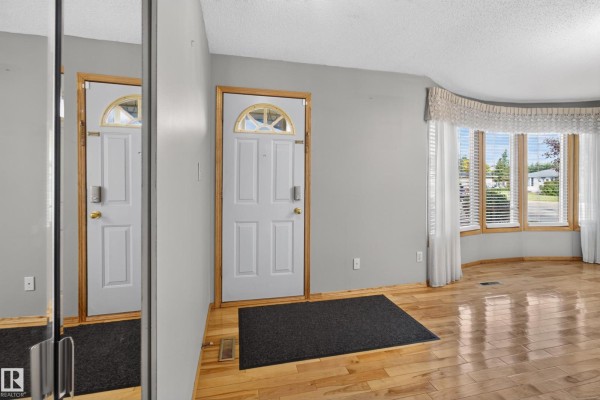 Interior entryway with white door, black mat, and wood floor reflecting in a mirror. - 13315 30 St Nw, Edmonton