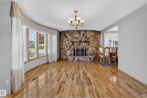 Living room with a stone fireplace, bay windows, chandelier, and adjacent dining area. - 13315 30 St Nw, Edmonton