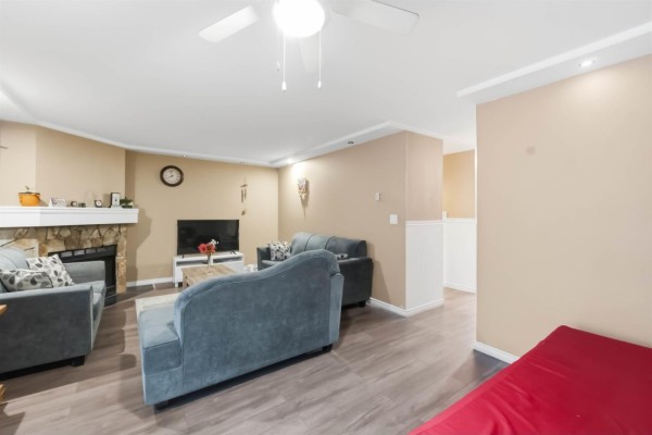 Living room with beige walls, stone fireplace, television, and view towards stairs. - 13323 71b Avenue, Surrey