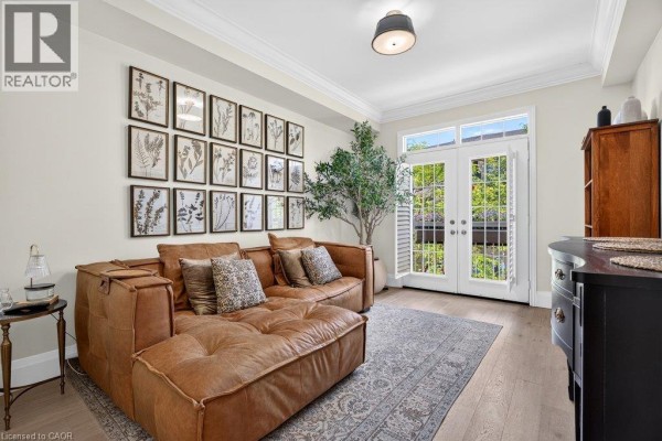 Living room with a large brown sectional sofa, a wall of botanical prints, and double glass doors. - 1335 Ontario Street Unit# 12, Burlington