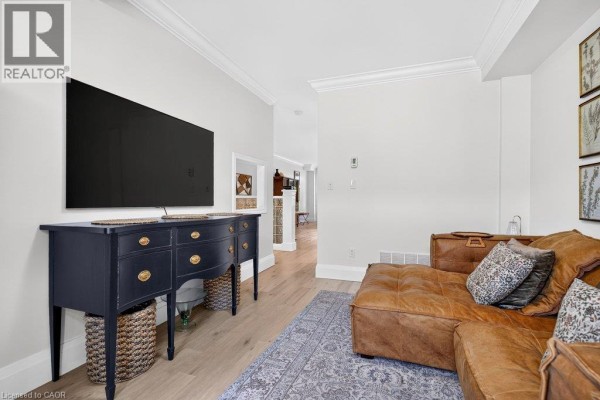 Living room with a dark blue dresser holding a TV, a brown sectional sofa, and a patterned rug. - 1335 Ontario Street Unit# 12, Burlington