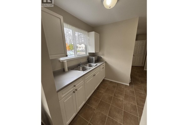 Kitchen with white cabinets, a double sink, grey countertops, and brown tiled floor. - 1335 Tweedsmuir Avenue, Kitimat
