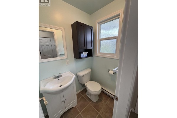 Bathroom with a pedestal sink, white toilet, dark wood cabinet, and light blue walls. - 1335 Tweedsmuir Avenue, Kitimat