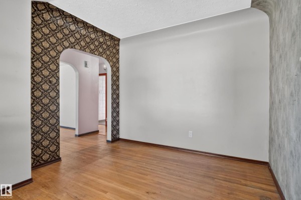 Interior view looking through an arched doorway with patterned wallpaper into a hallway and adjacent rooms. - 13351 109a Av Nw, Edmonton