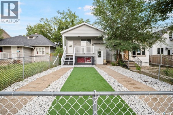 Front yard view of the house from behind a chain-link fence, with gravel and artificial turf. - 1337 Athol Street, Regina