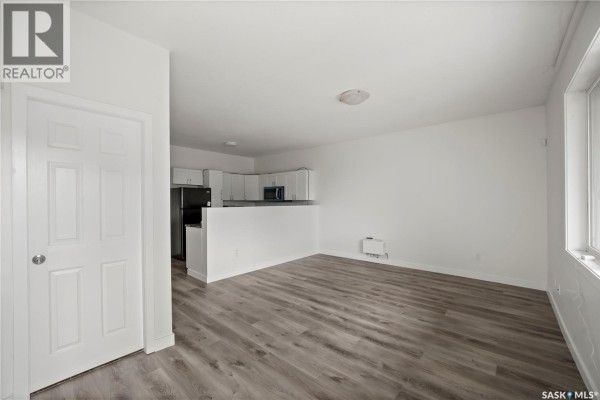 Interior view of a living room with white walls, grey wood-look flooring, and a doorway. - 1337 Athol Street, Regina