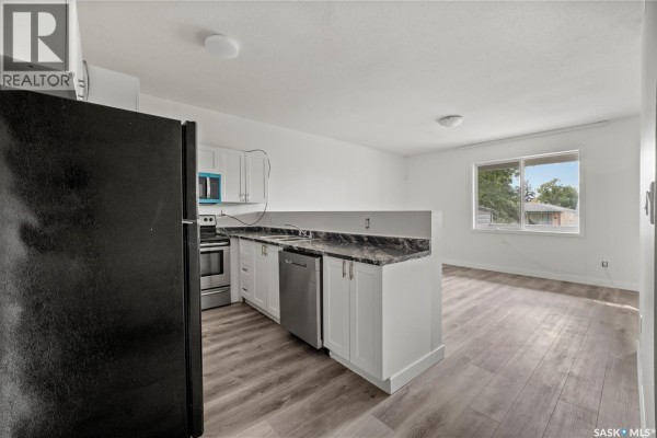 Kitchen area with white cabinets, black countertops, stainless steel appliances, and an open view to the living area. - 1337 Athol Street, Regina